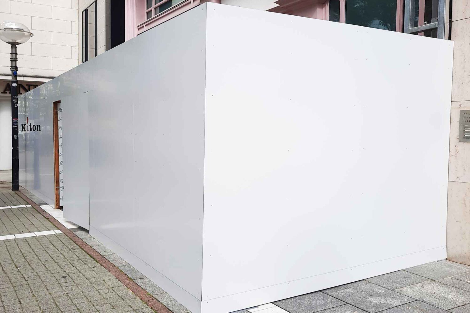 Bauzaun-mit-Verbundplatten-weiss Bauzaun aus Holzkonstruktion für Kiton auf der Goethestrasse in Frankfurt